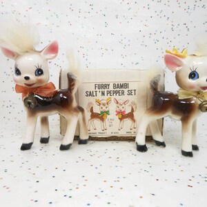May include: A vintage salt and pepper set featuring two ceramic deer figurines. The deer have white fur, brown bodies, and wear bells around their necks. The box reads "Furry Bambi Salt 'n Pepper Set."