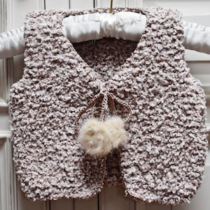 May include: A brown knitted waistcoat with a fluffy white pom-pom on the front.