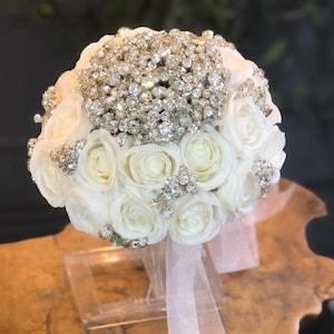 May include: A white bridal bouquet made of artificial roses and adorned with sparkling rhinestones.