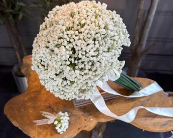 May include: A white bridal bouquet made of baby's breath flowers with a white satin ribbon. A matching boutonniere is also included.