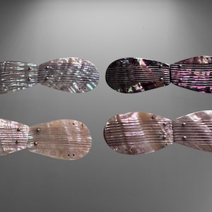 以下が含まれることがあります： 4つの蝶ネクタイ型のイリデセントヘアクリップ。各クリップは、水平なエッチングラインと小さな金属リベットを備えた貝殻素材で作られています。色はシルバーからピンク、パープルまであります。