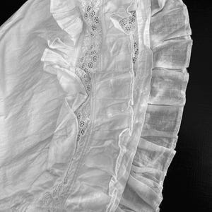 May include: A white cotton garment with a lace trim and multiple layers of ruffles.
