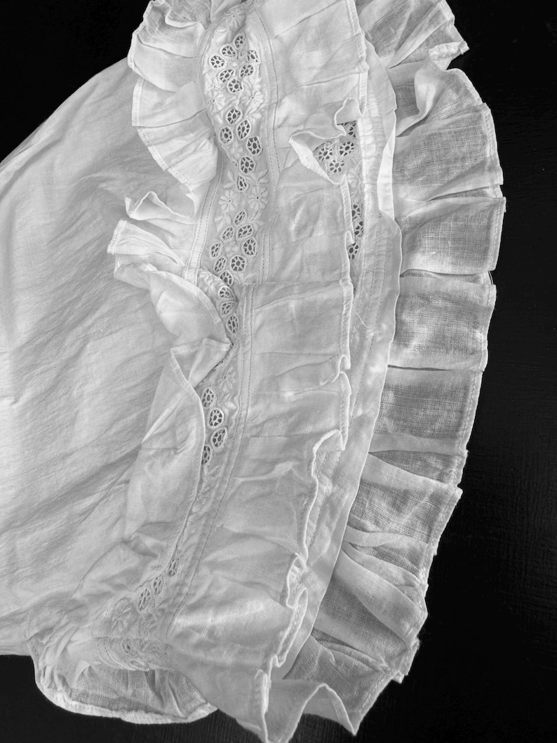 May include: A white cotton garment with a lace trim and multiple layers of ruffles.