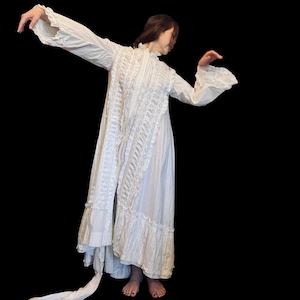 May include: A white, long-sleeved, lace-trimmed dress with a ruffled hem. The dress is flowing and has a vintage style.