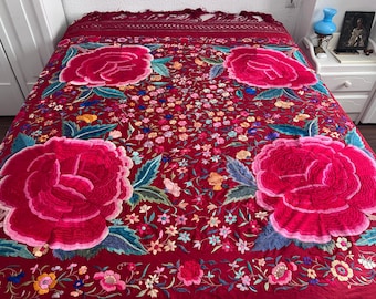 Peut inclure: Un châle rouge brodé avec un motif floral composé de grandes roses roses et de petites fleurs dans des tons de rose, bleu et jaune.