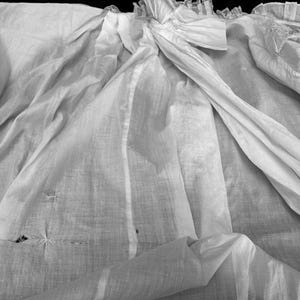May include: A white cotton fabric with a delicate lace trim. The fabric is wrinkled and has a few small holes.