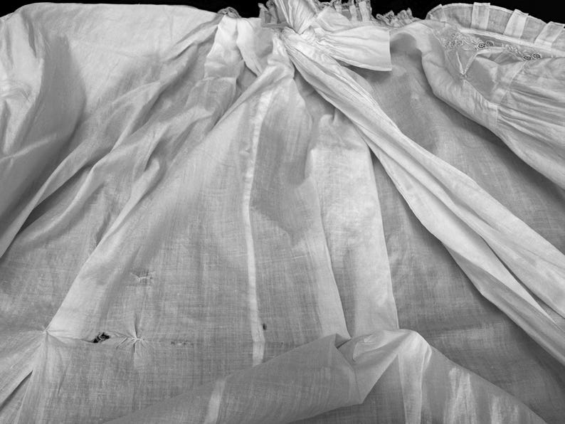May include: A white cotton fabric with a delicate lace trim. The fabric is wrinkled and has a few small holes.