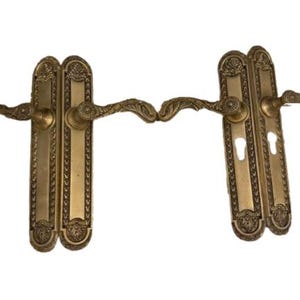 May include: Two antique brass door handles with ornate floral detailing. Each handle set includes a long rectangular backplate with a keyhole and a curved handle. The handles are a warm gold color.