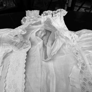 May include: A white cotton garment with delicate lace trim. The garment has a gathered neckline and a flowing, loose fit.