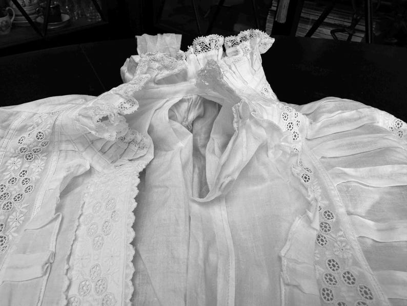 May include: A white cotton garment with delicate lace trim. The garment has a gathered neckline and a flowing, loose fit.