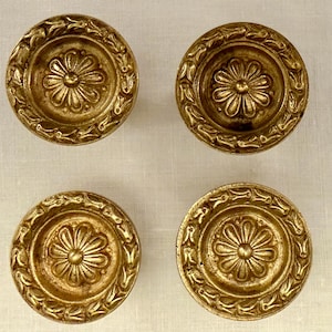 Può includere: Quattro pomelli antichi in ottone dorato con un design floreale. Ogni pomello presenta un fiore centrale circondato da un bordo dettagliato. I pomelli hanno una calda finitura dorata invecchiata.