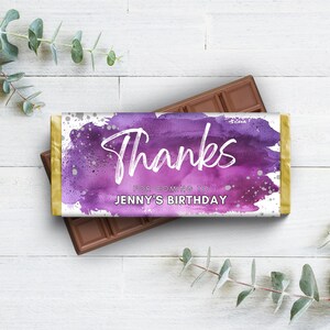 May include: A chocolate bar with a purple and white wrapper. The wrapper says "Thanks" in white script, with "For coming to Jenny's Birthday" below. The bar is on top of another chocolate bar.