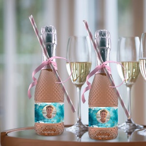 May include: Two small bottles of sparkling wine with personalized labels. The labels feature a blue watercolor background with gold accents and a photo of a person. The labels also include the text "Thanks for coming".