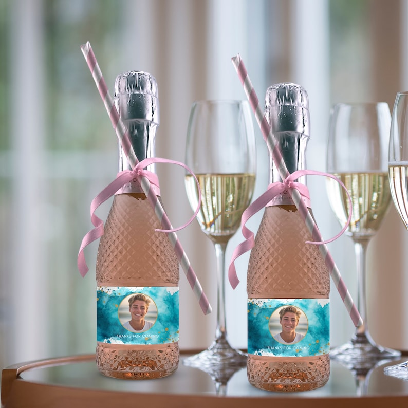 May include: Two small bottles of sparkling wine with personalized labels. The labels feature a blue watercolor background with gold accents and a photo of a person. The labels also include the text "Thanks for coming".