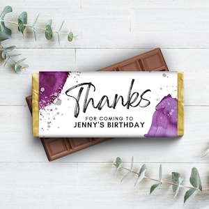 May include: A chocolate bar with a custom wrapper. The wrapper has the word "Thanks" in a handwritten font, with the text "FOR COMING TO JENNY'S BIRTHDAY" below. Purple watercolor accents and silver speckles decorate the wrapper.