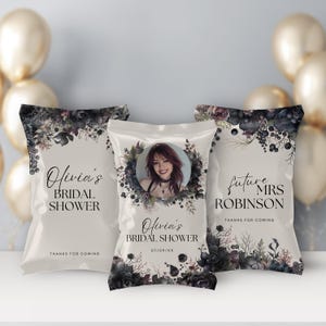 May include: Three white favor bags with black floral designs and the text "Olivia's Bridal Shower" and "Future Mrs. Robinson" with a photo of a woman in the center bag.