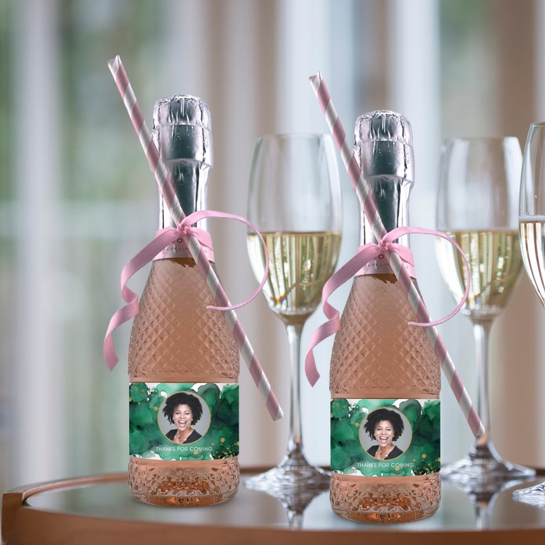 Op de afbeelding: Twee mini-flessen mousserende wijn met gepersonaliseerde etiketten. De etiketten hebben een groene aquarel achtergrond met gouden accenten en een foto van een persoon. De tekst op de etiketten luidt "Bedankt voor je komst".
