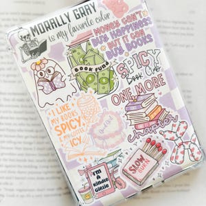 May include: A clear phone case with a checkerboard pattern and various stickers. Stickers include a skeleton reading, a ghost reading, stacks of books, and text that says "Morally Gray is my favorite color" and "Spicy Book Club."