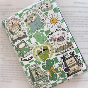 Peut inclure: Une coque transparente avec un motif à carreaux verts et blancs, ornée de divers autocollants. Les autocollants incluent une grenouille lisant un livre, une marguerite, un canard avec des livres et du texte qui dit "BOOKISH GIRLIE ERA" et "ANOTHER BOOK".