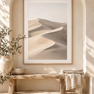May include: A framed vertical wall art print featuring a desert landscape with rolling sand dunes in shades of beige, tan, and soft gray. The image displays a clear horizon line under a pale sky, captured with high contrast between light and shadow.
