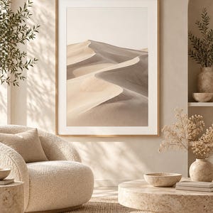May include: A framed vertical wall art print featuring a desert landscape with rolling sand dunes in shades of beige, tan, and soft gray, displayed in a light wood frame with a wide white mat border.