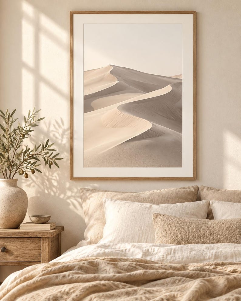 May include: A framed wall art print featuring a desert landscape with rolling sand dunes in shades of beige, tan, and soft gray. The image displays a high-contrast view of curved sand ridges under a bright, clear sky, enclosed in a light wood frame.