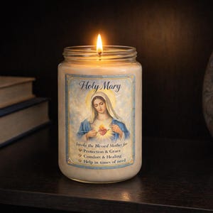 Op de afbeelding: Een brandende kaars in een glazen pot met een etiket met een afbeelding van de Maagd Maria. Het etiket leest "Holy Mary" en bevat tekst over bescherming, genade, troost en genezing. De kaars staat op een donkere ondergrond.