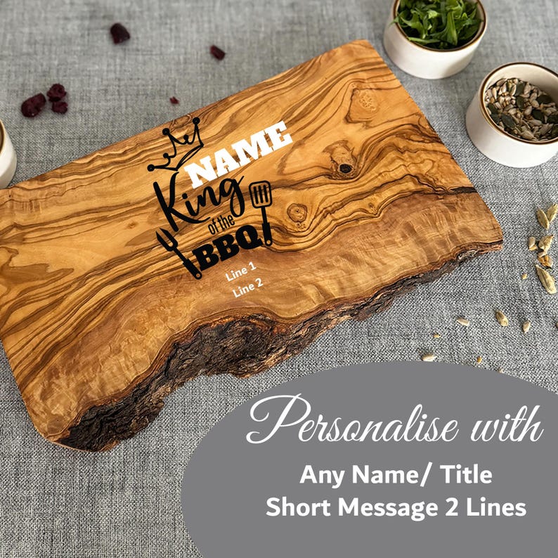 Puede incluir: Una tabla de cortar de madera con borde natural, con el texto "King of the BBQ" y espacio para personalizaci&oacute;n. La tabla es de color marr&oacute;n claro con bordes marrones oscuros y veta de madera natural. Incluye una corona y un gr&aacute;fico de herramientas de barbacoa.