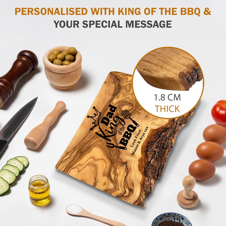 Puede incluir: Una tabla de cortar de madera con el texto "Dad King of the BBQ!" y un gr&aacute;fico de corona. La tabla tiene 1,8 cm de grosor y est&aacute; rodeada de ingredientes y utensilios de cocina, como aceitunas, huevos y un cuchillo.