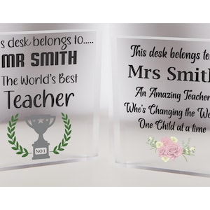 Pu&ograve; includere: Due blocchi da scrivania in acrilico trasparente con messaggi personalizzati per gli insegnanti. Il primo blocco dice "Questa scrivania appartiene a... MR SMITH Il miglior insegnante del mondo" con un trofeo e una corona di alloro. Il secondo blocco dice "Questa scrivania appartiene a... Sig.ra Smith Un'insegnante straordinaria che sta cambiando il mondo un bambino alla volta" con fiori rosa.