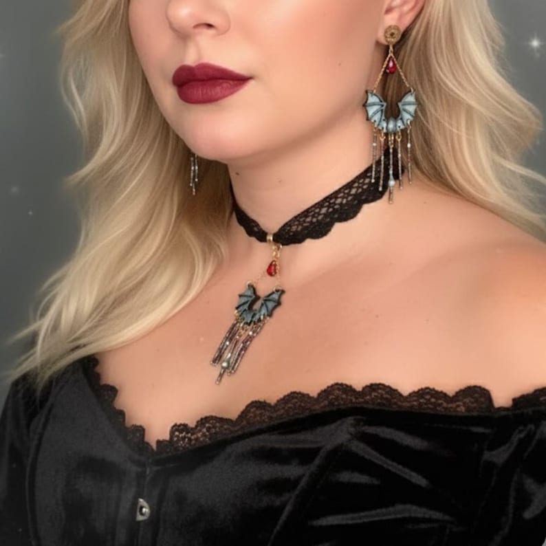 Modelo usando un set de pendientes y choker hechos a mano con diseño de murciélago y cuentas colgantes en tonos negro, gris y rojo. Lleva un top negro de encaje sobre fondo gris con destellos suaves.