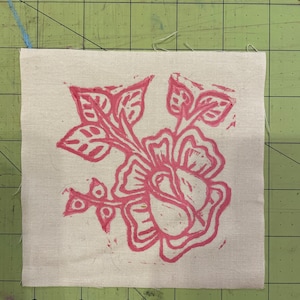 Pode incluir: Um desenho floral rosa impresso em um tecido bege. O desenho apresenta uma flor grande com v&aacute;rias p&eacute;talas e folhas.
