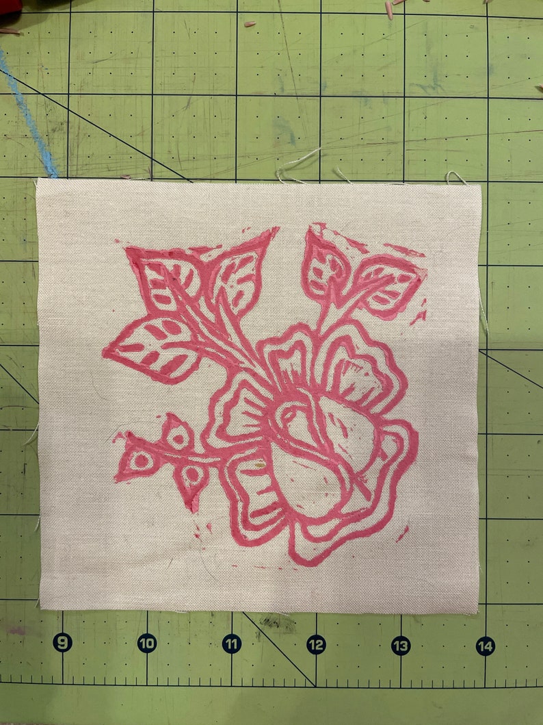 Pode incluir: Um desenho floral rosa impresso em um tecido bege. O desenho apresenta uma flor grande com v&aacute;rias p&eacute;talas e folhas.