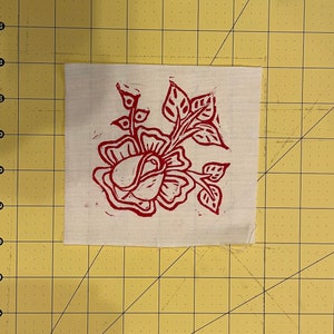 Pode incluir: Um desenho floral vermelho impresso em um quadrado de tecido branco.