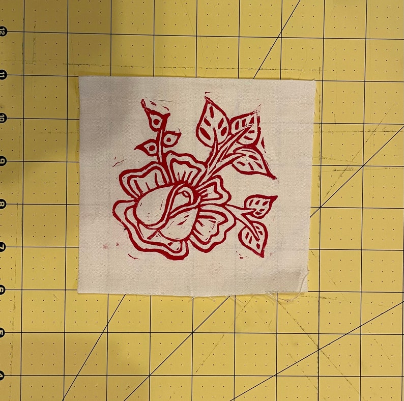 Pode incluir: Um desenho floral vermelho impresso em um quadrado de tecido branco.