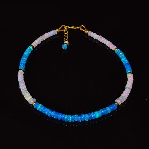 May include: A delicate necklace made of alternating blue and white opal beads with gold accents. The necklace is strung on a gold chain with a lobster clasp.