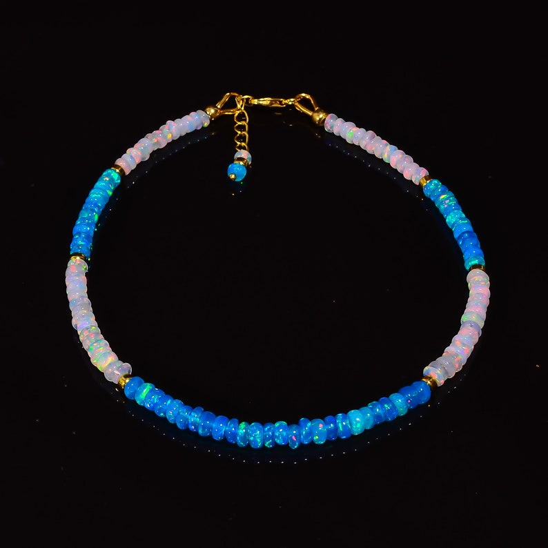 May include: A delicate necklace made of alternating blue and white opal beads with gold accents. The necklace is strung on a gold chain with a lobster clasp.
