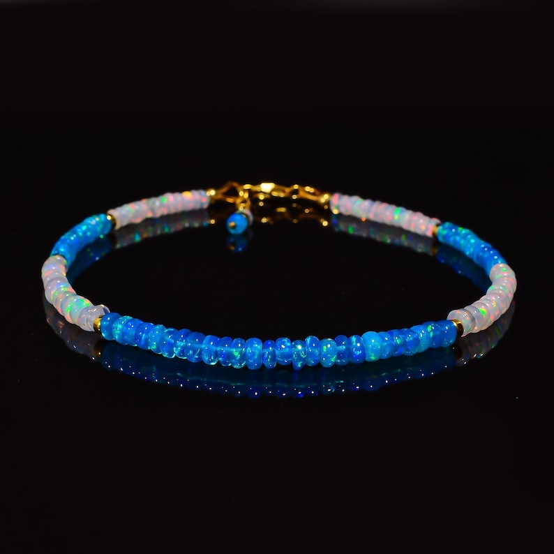 May include: A delicate bracelet made with blue and white opal beads. The bracelet has a gold clasp and is perfect for adding a touch of elegance to any outfit.