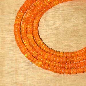 May include: A strand of orange opal beads, with a slight iridescent sheen, is arranged in a circle on a wooden surface.