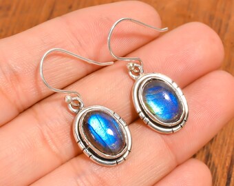 May include: A pair of silver earrings with oval-shaped blue labradorite gemstones. The earrings have a simple design with a silver wire loop and a small silver bead at the top.