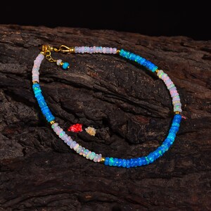 May include: A delicate gold chain necklace with alternating white and blue opal beads. The necklace is displayed on a piece of wood.