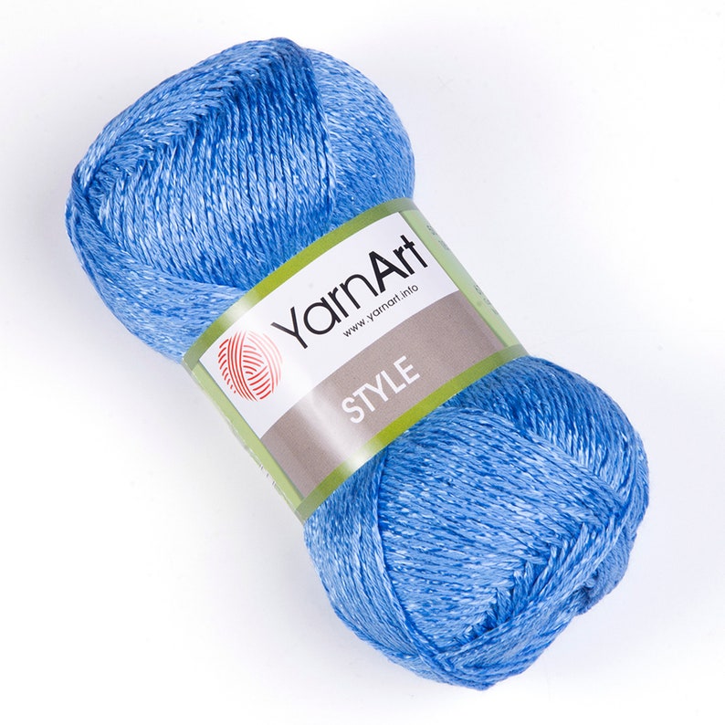 Pode incluir: Uma meada de fio azul claro com acabamento brilhante. O fio &eacute; etiquetado com "YarnArt" com o endere&ccedil;o do site "www.yarnart.info" e a palavra "STYLE" impressa no r&oacute;tulo.