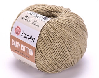 Pode incluir: Uma bola de fio bege com a etiqueta "YarnArt Baby Cotton" com as informações de peso e comprimento: 50g / 1,76 oz, 165 m / 180,44 yds.