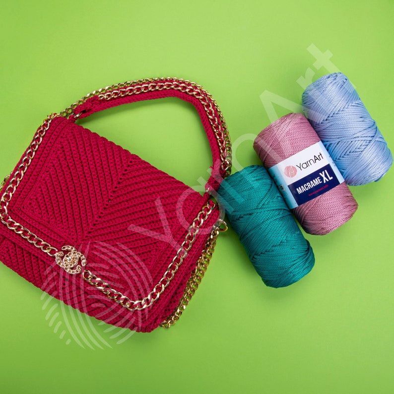 May include: A red crocheted handbag with a gold chain strap and a gold clasp. Three balls of yarn in pink, blue, and teal are next to the bag. The yarn is labeled "YarnArt Macrame XL."