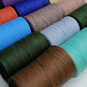 May include: A collection of spools of colorful paper twine. The spools are arranged in a row, with the colors ranging from yellow to green to brown. The twine is made of thin strips of paper that are twisted together.
