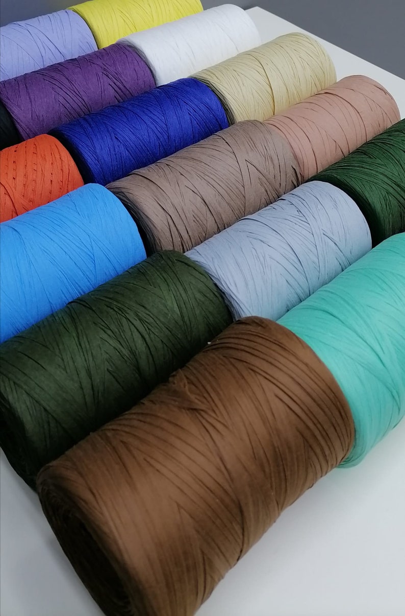 May include: A collection of spools of colorful paper twine. The spools are arranged in a row, with the colors ranging from yellow to green to brown. The twine is made of thin strips of paper that are twisted together.