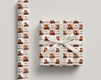 May include: Gift wrap and a wrapped present with a white ribbon. The paper has a repeating pattern of a person's image and the text "ITS A GIFT". The wrapped gift is also covered in the same pattern.