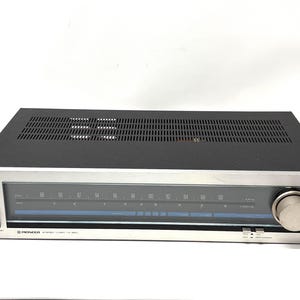 May include: A vintage Pioneer stereo tuner with a silver face and black top. The tuner features a dial with frequency markings, a power button, and a large tuning knob. The model number TX-500L is visible.