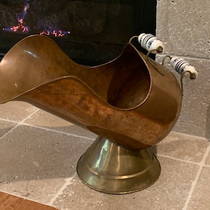 May include: A copper fireplace tool with a brass base and two white porcelain handles with blue floral designs.