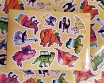 May include: A sheet of stickers featuring various dinosaurs with different pride flags. The dinosaurs are in various poses, some holding flags, some wearing flags, and some with flags behind them. The flags include the bisexual, lesbian, transgender, non-binary, and pansexual flags.